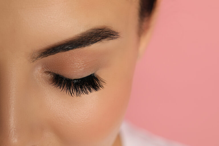 Kobieta z długimi, podkręconymi rzęsami na różowym tle – BelleLashes